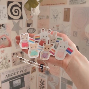 May include: A set of six colorful stickers featuring cartoon animals with rainbow flags. The animals are a cat, a rabbit, a bear, a deer, a rabbit, and a cat. The text on the sticker reads "Customs for other flags available, send me a message! :)"