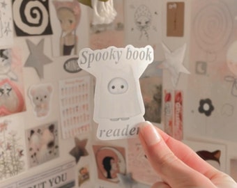 Könnte beinhalten: Ein weißer Geisteraufkleber mit dem Text "Spooky book reader" auf weißem Hintergrund. Der Aufkleber befindet sich an einer Wand mit anderen Aufklebern.