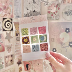 May include: A sheet of decorative stickers featuring nine square designs in various colors and patterns. The stickers include floral, geometric, and celestial motifs. The text "bloom sweet" is printed at the top.