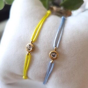 May include: Two bracelets with a single clear rhinestone on each. One bracelet is yellow and the other is light blue.