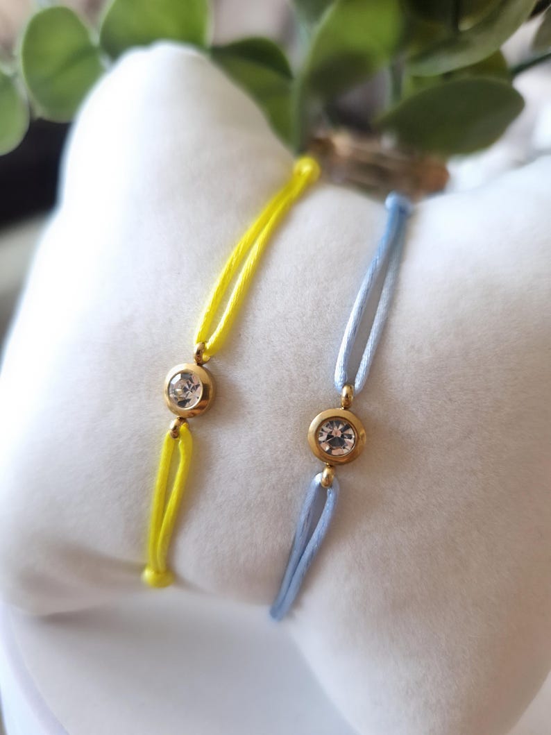 May include: Two bracelets with a single clear rhinestone on each. One bracelet is yellow and the other is light blue.