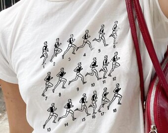 May include: White t-shirt featuring a black graphic of a runner's stride sequence, numbered 1 through 18. The shirt is paired with gray pants and a brown belt. A red purse is visible on the right side.