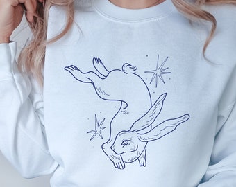 May include: A light blue sweatshirt with a blue line drawing of a rabbit with wings and stars on the front.