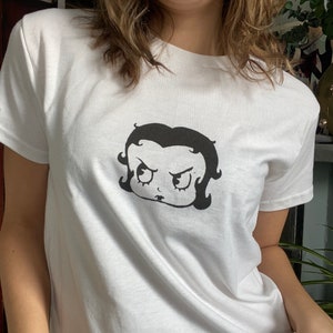 May include: White t-shirt with a black and white cartoon image of a girl with an angry expression.