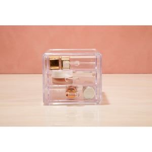May include: A clear plastic drawer organiser with three drawers. The drawers are filled with various small items, including a gold bottle, a white bottle, and a silver lid.