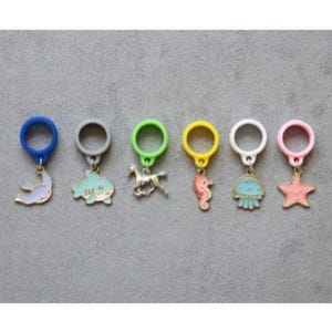 May include: Six colorful silicone rings with different sea creature charms. The charms include a shark, a seahorse, a jellyfish, a starfish, a dolphin, and a horse.