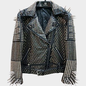 May include: Black leather jacket heavily embellished with silver studs and spikes. The jacket features a classic asymmetrical zip closure, notched lapels, and a belted waist. The sleeves and shoulders are adorned with long, pointed spikes.