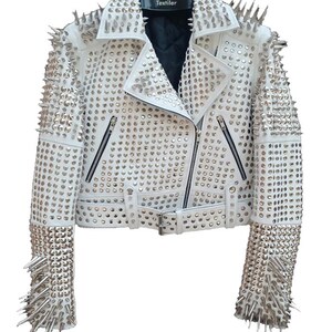 May include: White leather jacket with silver metal studs and spikes. The jacket features a notched collar, a zipper closure, and multiple pockets. The sleeves and shoulders are heavily embellished with studs and spikes, creating a bold, edgy look.