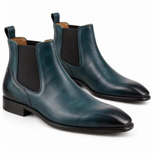 Könnte beinhalten: Ein Paar blaugrüne Chelsea-Boots aus glattem Leder mit einem dunklen Farbverlauf an der abgerundeten Schuhspitze. Diese Stiefeletten verfügen über schwarze elastische Seiteneinsätze, eine Zugschlaufe an der Ferse und einen flachen schwarzen Absatz.