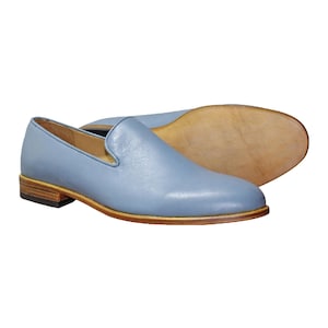 Op de afbeelding: Een paar lichtblauwe leren loafers met een gladde afwerking, een laag profiel, een beige gestapelde houten hak en een lichtbruine leren zool. De schoenen hebben een eenvoudig instapmodel met een ronde neus en een strak, onversierd bovenwerk.