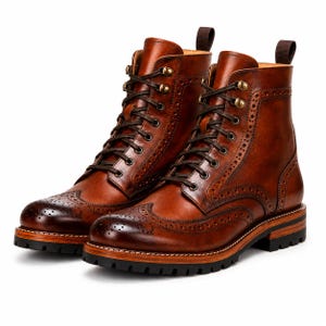 May include: A pair of brown leather lace-up boots featuring brogue detailing, a wingtip toe cap, and dark brown laces. The boots have brass-toned metal eyelets, a stacked wooden midsole, and a thick black lugged rubber outsole with a pull tab.