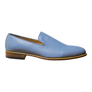 Op de afbeelding: Een lichtblauwe leren loafer met een gladde afwerking, voorzien van een laag profiel, een beige leren tussenzool en een donkerbruine gestapelde hak. De binnenvoering is lichtbeige en de schoen heeft een afgeronde neus.