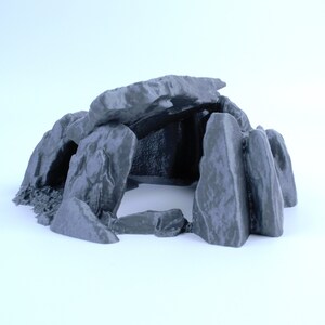 Può includere: Una formazione rocciosa grigia stampata in 3D con un'apertura di grotta. La grotta è formata da diverse rocce impilate l'una sull'altra, creando un piccolo spazio chiuso.