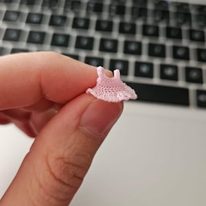 May include: A small pink crocheted dress, held in a hand.