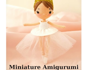 May include: A handmade amigurumi ballerina doll, featuring a white tutu and a gold crown. The doll has a light skin tone and brown hair. The text "Miniature Amigurumi Pattern Ballerina Bella" is displayed below the doll.
