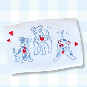 May include: A white baby blanket with blue embroidered dogs and red hearts. The dogs are carrying hearts and one is holding a heart in its mouth.