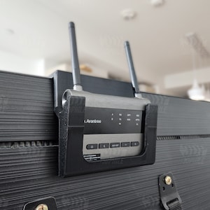 May include: A black and silver wireless HDMI transmitter with two antennas, mounted on a black surface. The transmitter has a label that reads "Avantree".