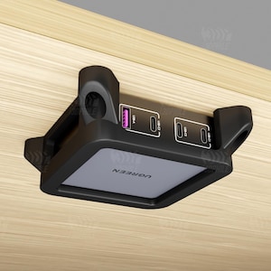 May include: A black UGREEN charging station with USB and USB-C ports, mounted under a wooden surface. The station has a gray top with the UGREEN logo and a purple USB port.