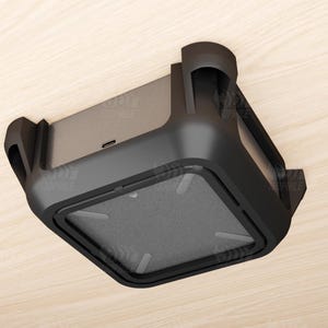 May include: A black charging dock with a rectangular base and rounded edges. The dock has a built-in charging port and a textured surface. The design includes two curved side supports and a sleek, modern aesthetic.