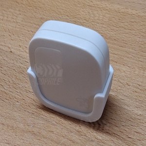 Può includere: Un dispositivo per la casa intelligente di colore bianco con una forma quadrata arrotondata. Il dispositivo è posizionato su una superficie di legno. Il dispositivo ha un piccolo logo sul davanti che dice "Tophile".