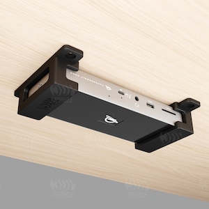 May include: A black device with multiple ports is mounted to the underside of a wooden surface using a black plastic bracket.