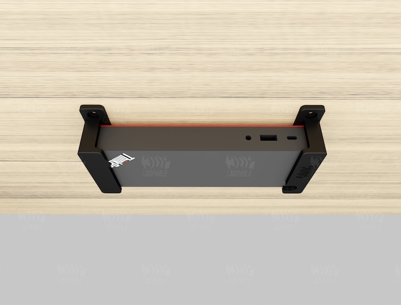 Puede incluir: Soporte de pared negro con un dispositivo negro fijado a &eacute;l. El dispositivo tiene una franja roja y algunos puertos en el lateral. El soporte est&aacute; fijado a una superficie de madera clara.