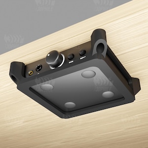 May include: A black audio amplifier with a volume knob, input and gain buttons, and multiple input jacks. The amplifier is mounted on a light wood surface.