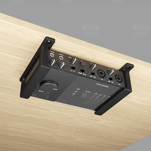 Könnte beinhalten: Ein schwarzes Audio-Interface mit Knöpfen und Tasten, das mit einer Halterung an einer Holzoberfläche befestigt ist.