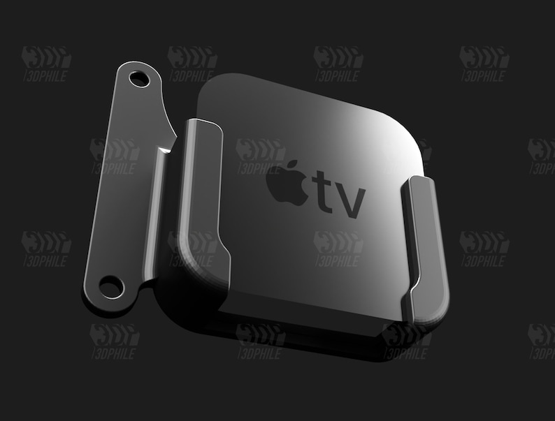 May include: A black metal wall mount for an Apple TV streaming device. The mount has a simple design with two arms that hold the device securely in place. The Apple TV is visible in the mount, with the Apple logo and the text "tv" displayed on the front.