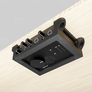 Puede incluir: Interfaz de audio negra con perillas y un dial grande, montada en una superficie de madera con soportes.