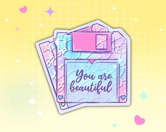 May include: A stack of three pastel-colored floppy disk stickers. Each sticker has a pink, blue, and purple design with the words "You are beautiful" in cursive. The background is a grid pattern with stars and hearts.