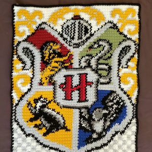 以下が含まれることがあります： ホグワーツの家の紋章が描かれた、かぎ針編みタペストリー。紋章は伝統的な色で描かれています。グリフィンドール（赤と金）、ハッフルパフ（黄色と黒）、レイブンクロー（青とブロンズ）、スリザリン（緑と銀）です。