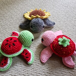 May include: Three crocheted turtle toys. One is green with a watermelon shell, one is pink with a strawberry shell, and one is gray with a sunflower shell.