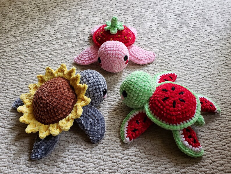 May include: Three crocheted turtle toys, each with a different fruit design. One is a pink strawberry turtle, one is a green watermelon turtle, and one is a gray sunflower turtle.