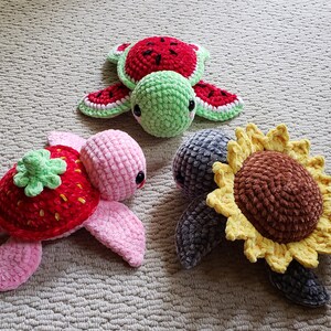 May include: Three crocheted turtle toys. One is pink with a strawberry on its back, one is green with a watermelon on its back, and one is gray with a sunflower on its back.