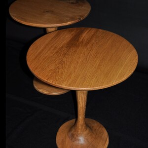 Könnte beinhalten: Zwei verschachtelte Holztische mit runden Tischplatten und einem einzigartigen, ausgestellten Fuß. Die Tische sind aus hellbraunem Holz mit einer natürlichen Oberfläche.