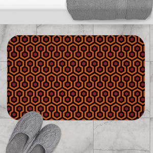 May include: A bath mat with a repeating geometric pattern of red and orange hexagons on a black background. The pattern is reminiscent of the Overlook Hotel carpet from the movie "The Shining".