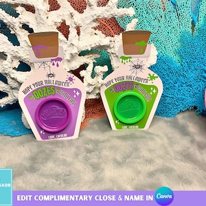 Puede incluir: Dos recipientes de Play-Doh con temática de Halloween con forma de botellas de poción. Uno es morado con tapa morada, el otro es verde con tapa verde. Cada uno tiene el texto "Hope Your Halloween Oozes With Fun!" y "Love, Lachman."