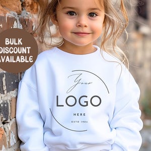 May include: A white sweatshirt with a custom logo design. The sweatshirt features a circular logo design with the text "Your Logo Here" and "ESTD 1984". The words "Bulk Discount Available" are in a brown circle.