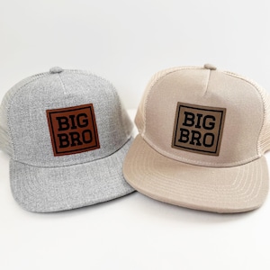 May include: Two trucker hats, one gray and one tan, each with a square leather patch that reads "BIG BRO" in bold, black letters. The hats have a mesh back and a curved brim.