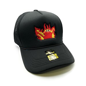 May include: Black trucker hat with a red and yellow embroidered flame design. The hat has a mesh back and a black brim. The hat also has a yellow label that says "Hatone Official Licensed Product".