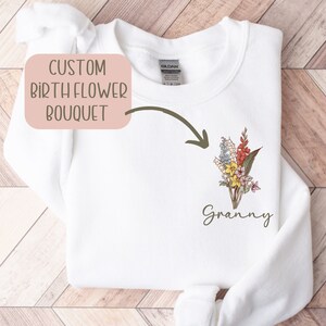 May include: White sweatshirt with a custom birth flower bouquet design and the word "Granny" printed below. The design features a bouquet of colorful flowers.