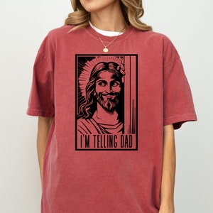 May include: Red t-shirt featuring a black and white image of Jesus with the text "I'm telling Dad" printed on the front.