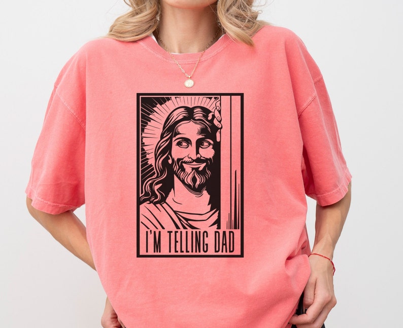 May include: A pink t-shirt featuring a black and white illustration of Jesus with the text "I'm telling Dad" underneath.