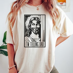 May include: A white t-shirt featuring a black and white illustration of Jesus with the text "I'm telling Dad".