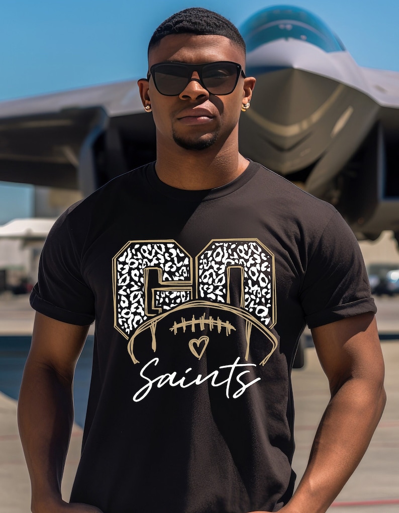 May include: Black t-shirt with a gold and white leopard print "GO Saints" design featuring a football with a heart.