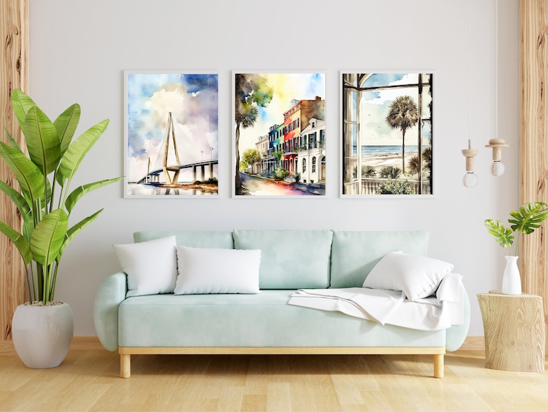 May include: Three watercolor paintings in white frames depicting scenes from Charleston, South Carolina. The first painting shows the Cooper River Bridge, the second shows a street lined with colorful houses, and the third shows a window view of a palm tree on the beach.