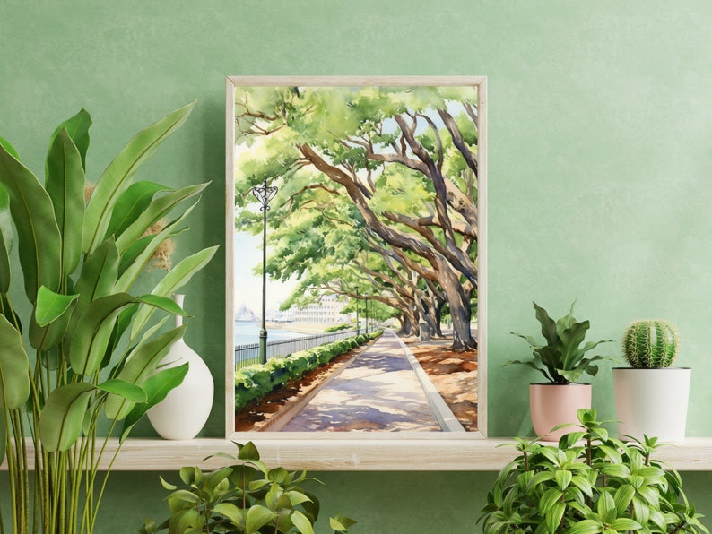 May include: A watercolor painting of a tree-lined path leading to a waterfront. The trees have lush green leaves and the path is shaded by the trees. The painting is framed in a light wood frame.