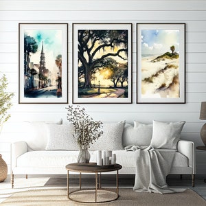 May include: Three framed watercolor paintings depicting scenes from a coastal town. The first painting shows a street with a church steeple in the background. The second painting shows a large oak tree with Spanish moss hanging from its branches. The third painting shows a beach scene with a palm tree and sand dunes.