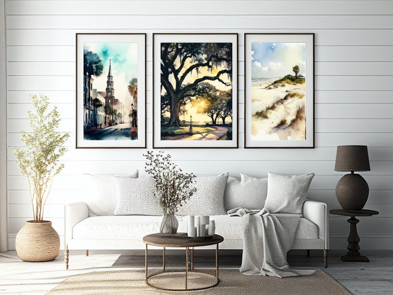May include: Three framed watercolor paintings depicting scenes from a coastal town. The first painting shows a street with a church steeple in the background. The second painting shows a large oak tree with Spanish moss hanging from its branches. The third painting shows a beach scene with a palm tree and sand dunes.